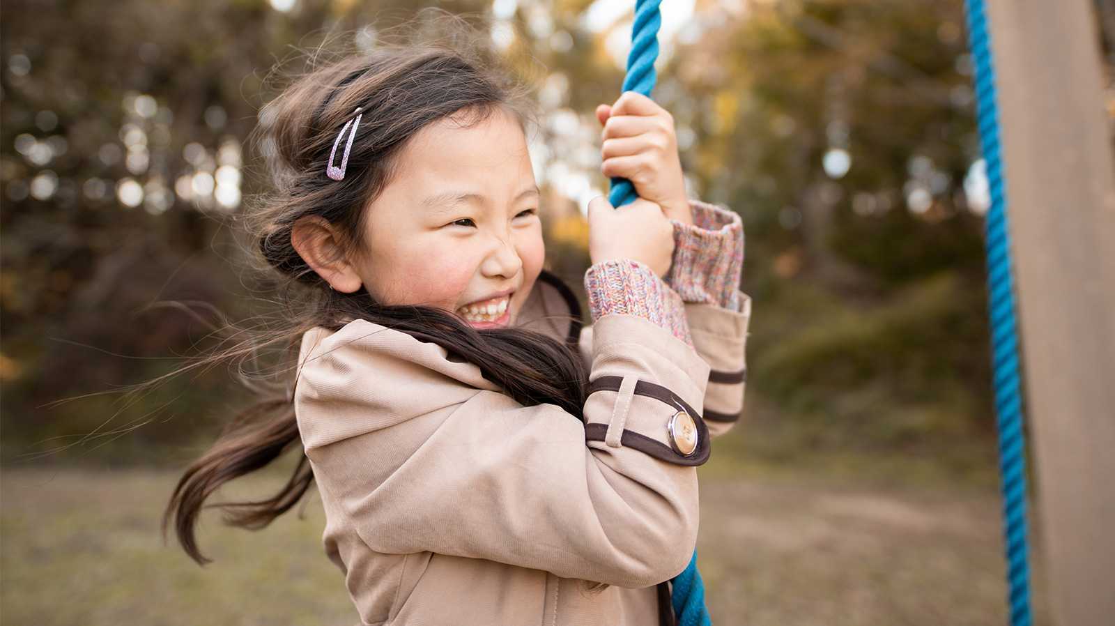 Smiling girl holding onto a playground rope.